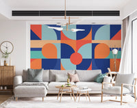 Modern geometric wall mural behind a grey sectional sofa in a bright room