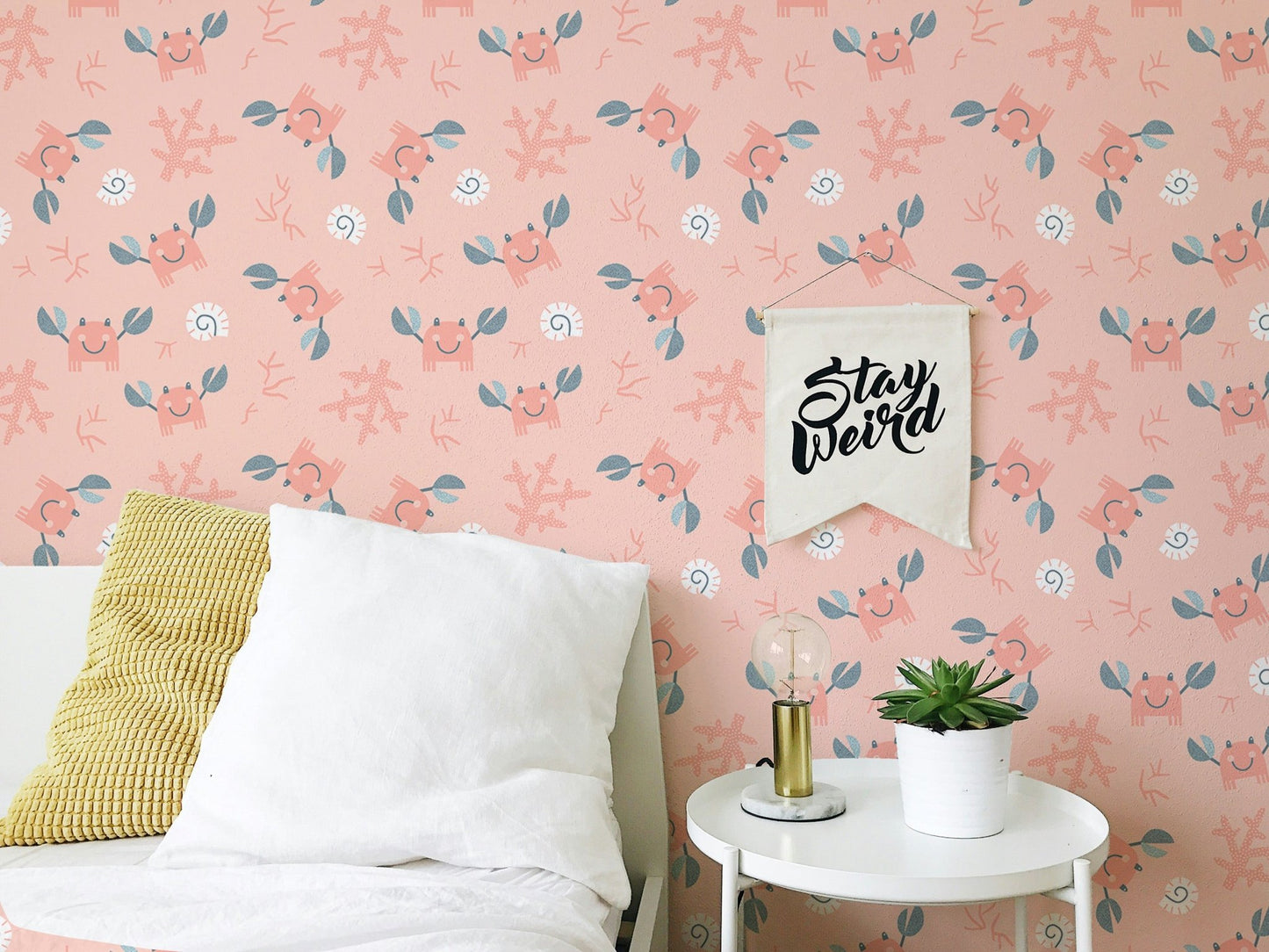 Pink marine life wallpaper in bedroom behind a white bed with a yellow cushion.
