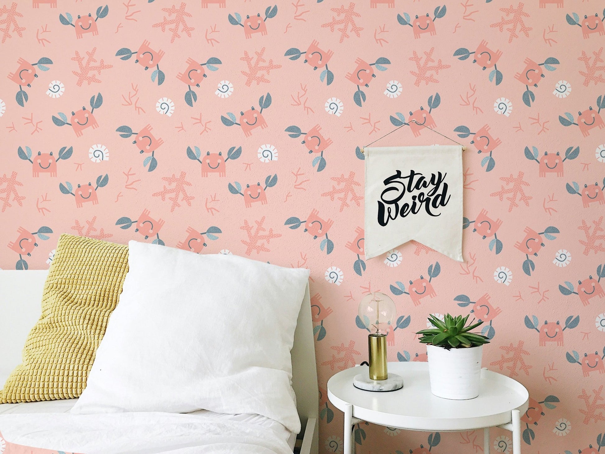 Pink marine life wallpaper in bedroom behind a white bed with a yellow cushion.