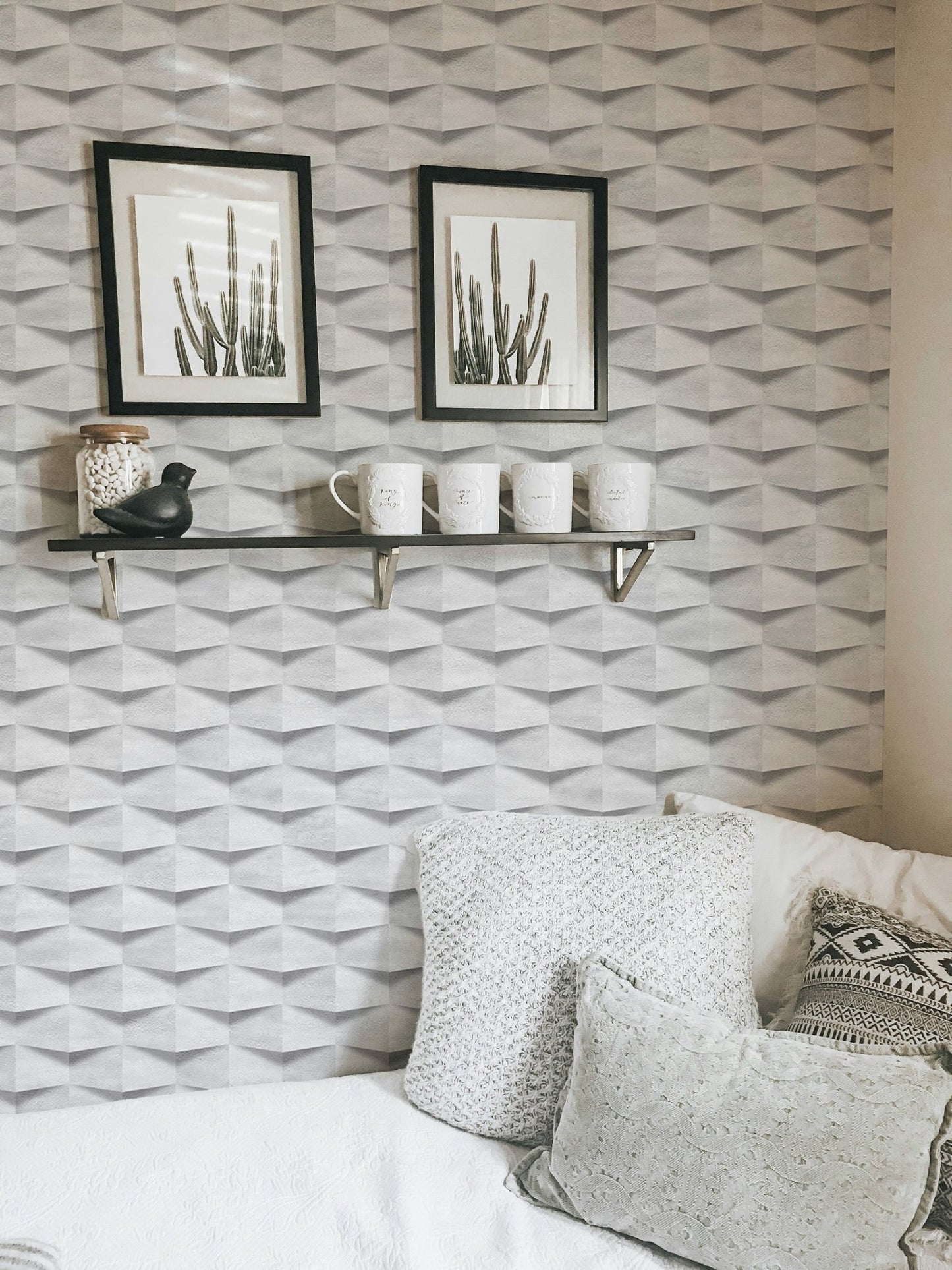 Textured abstract wallpaper behind white cushions and black framed cactus wall art.