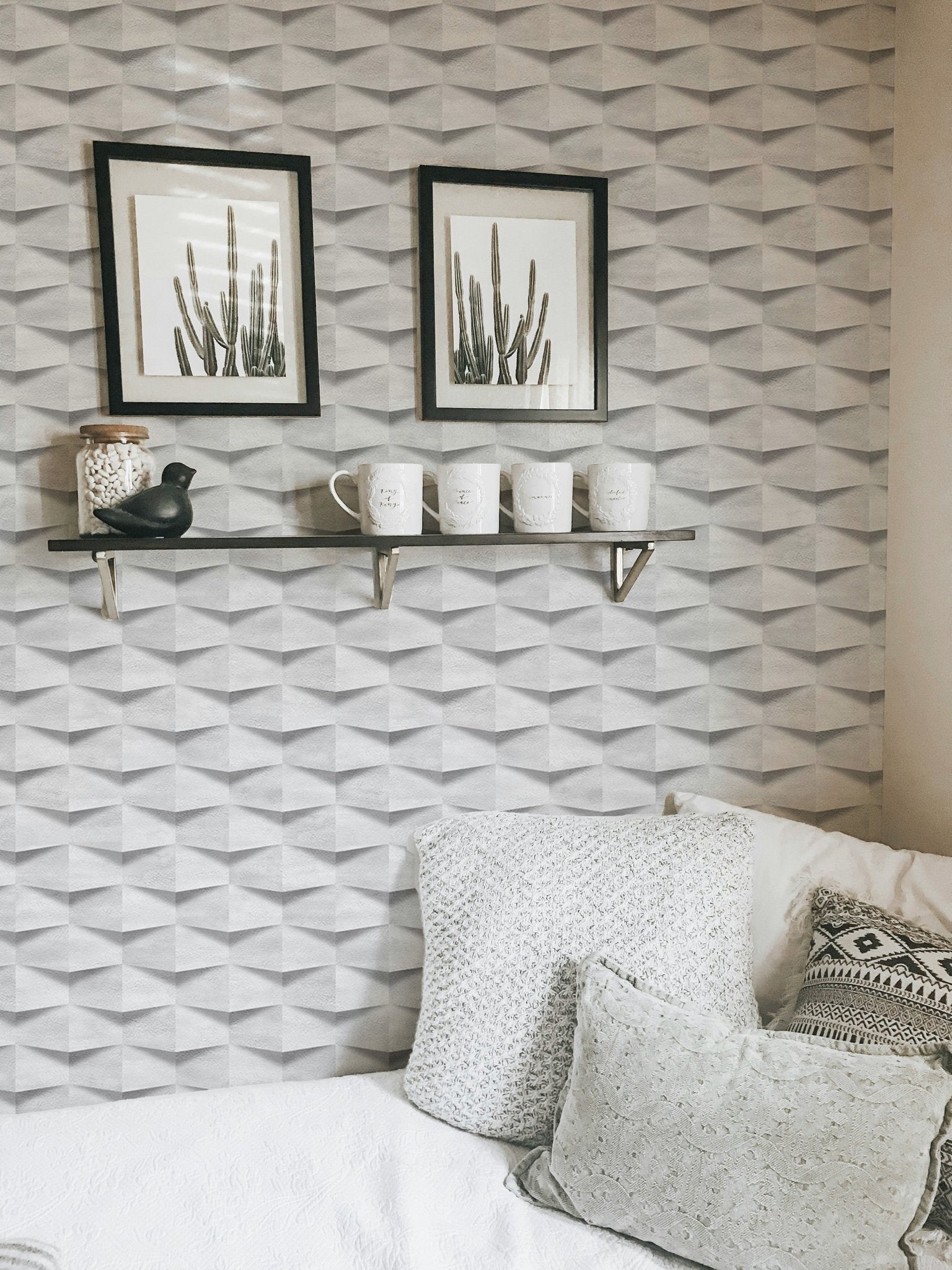 Textured abstract wallpaper behind white cushions and black framed cactus wall art.