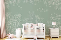 Sage green wall mural with white deer doodles in a nursery with a white crib.
