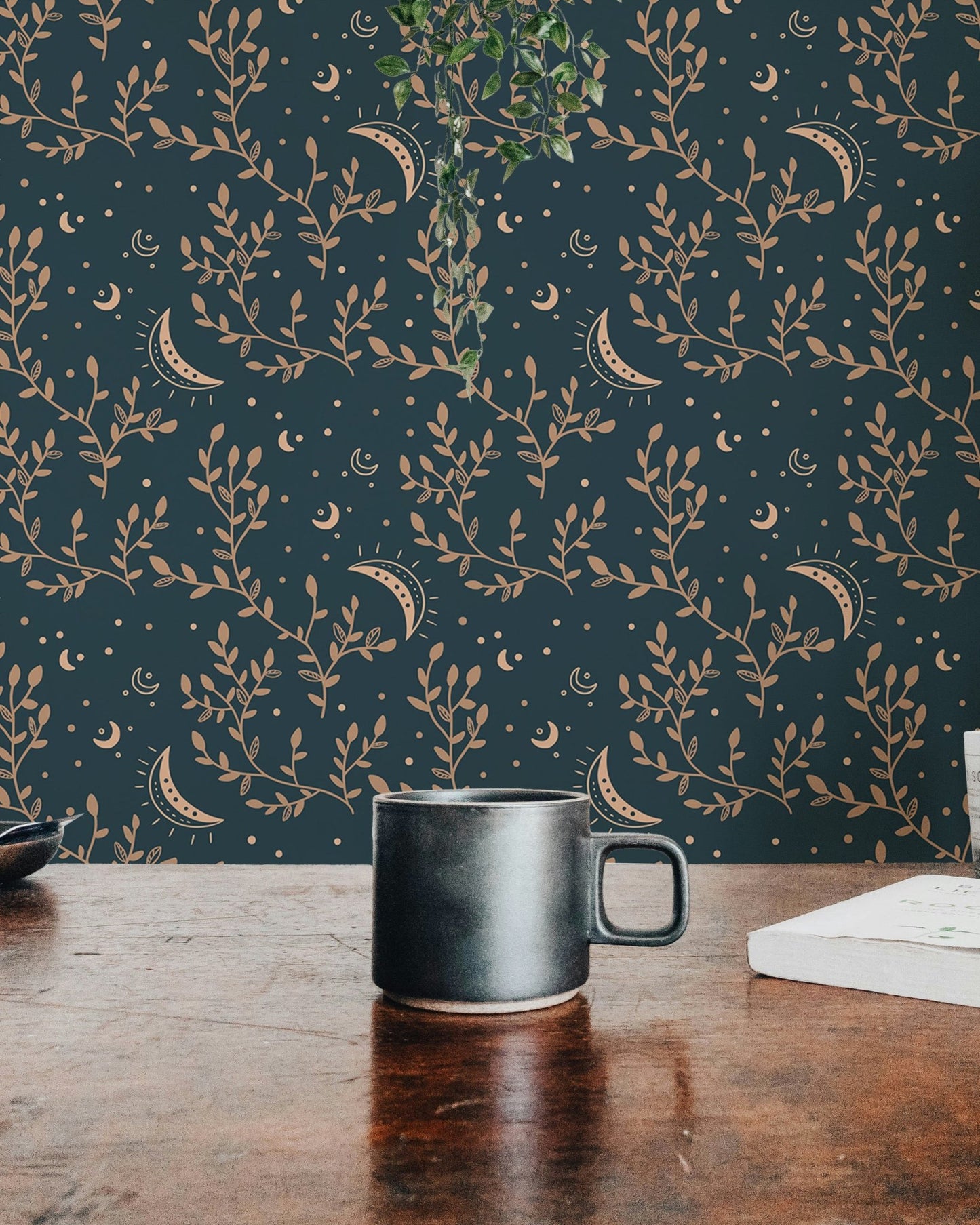 Dark teal wallpaper with gold celestial moon and floral patterns behind a coffee mug.