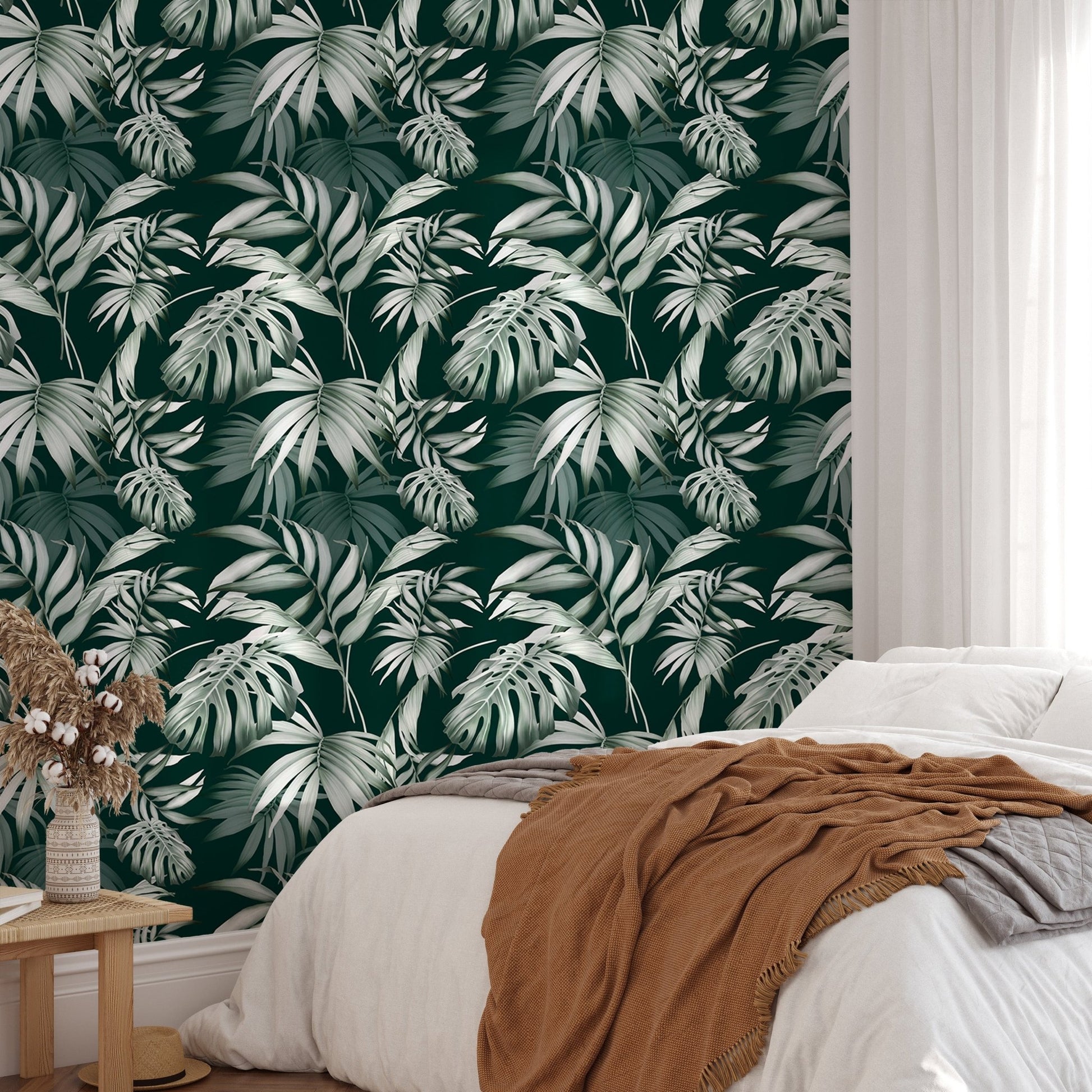Tropical leaf wallpaper behind a white bed with brown and grey linen.