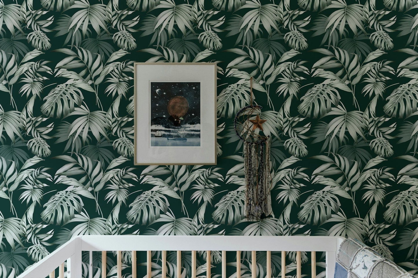 Jungle leaf wallpaper inside a nursery with a white crib and wall art.