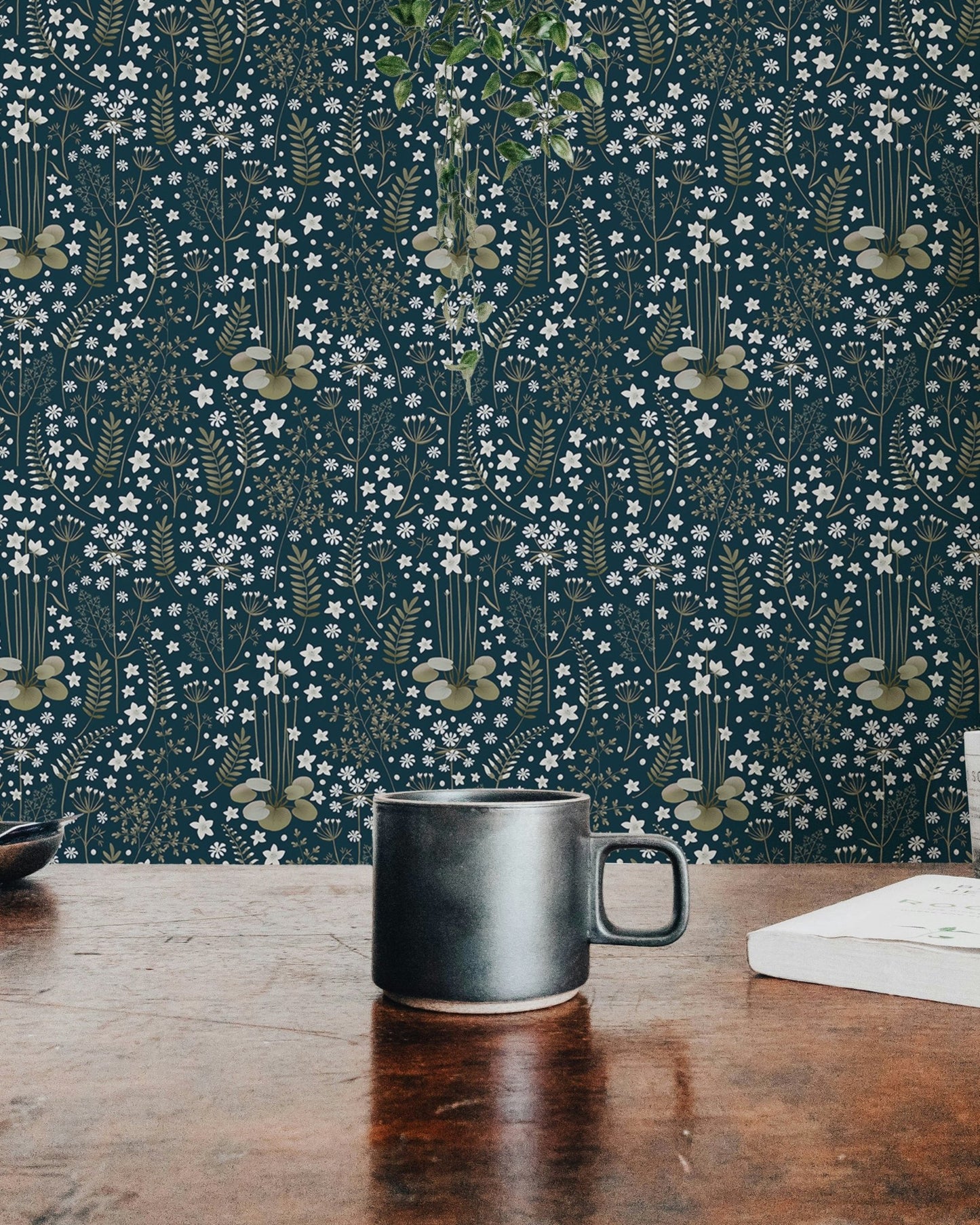 Detailed dark blue floral wallpaper behind a black coffee mug on a wooden table.