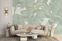 Green tropical foliage wall mural behind a beige sofa and gold pendant light in bright living room.