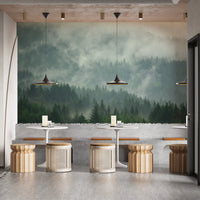 Misty forest mural in a cafe with round wooden stools and pendant lights.