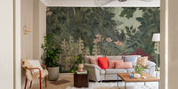 Green foliage wall mural in living area with grey sofa and red cushions.