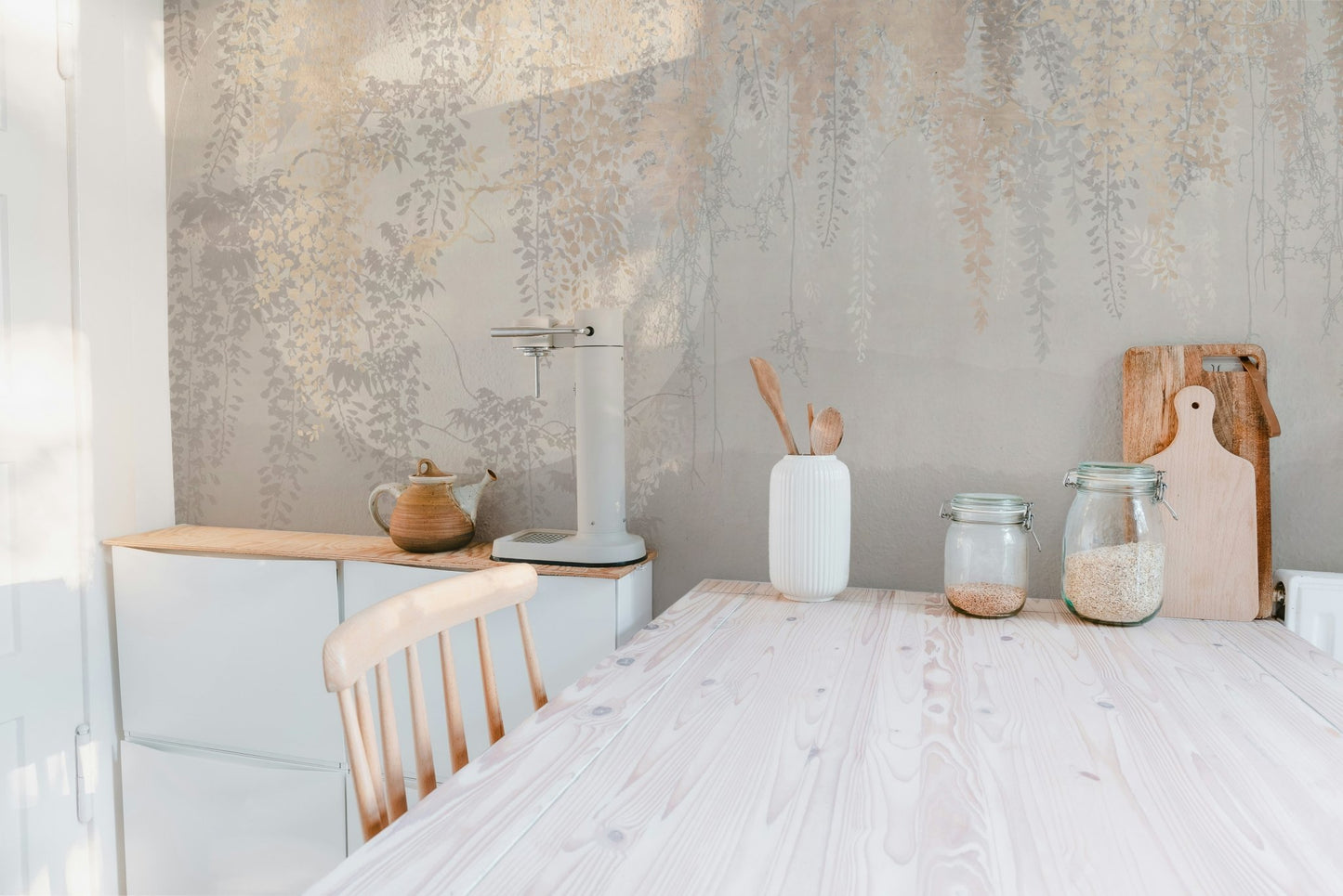 Kitchen wall mural with grey and gold botanical patterns behind a wooden table.
