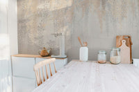 Kitchen wall mural with grey and gold botanical patterns behind a wooden table.