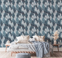 Gouache mountains houses scandinavian wallpaper behind bed with light blue linens.