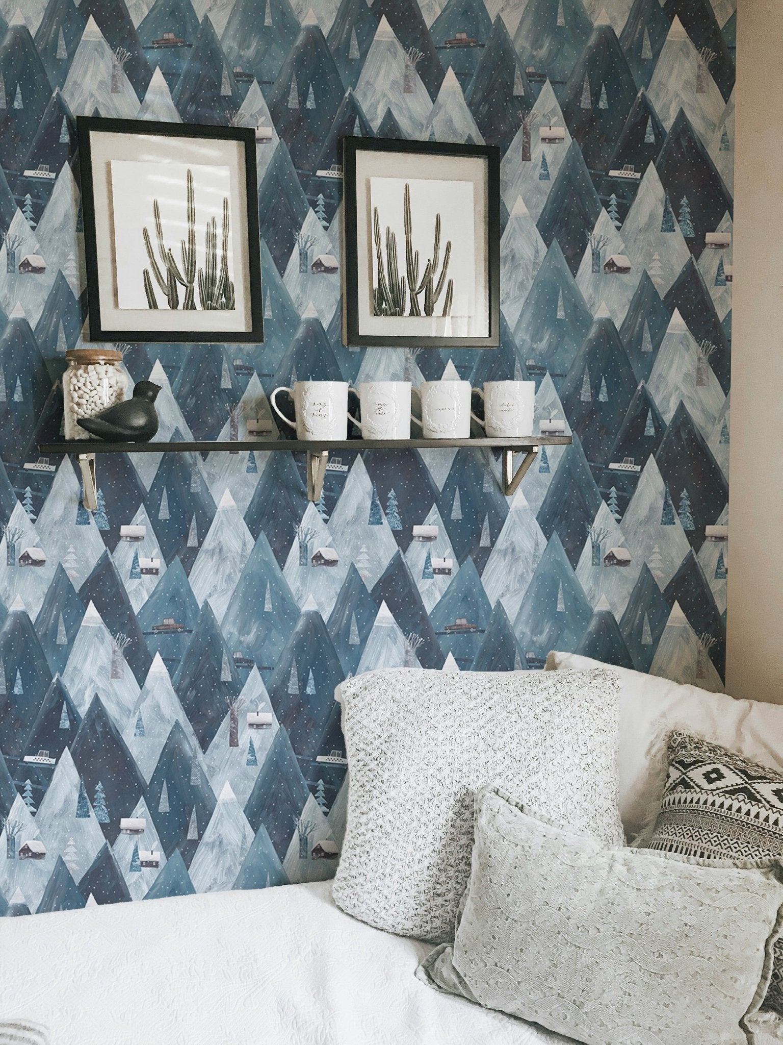 Geometric mountain wallpaper with black frames and white pillows in bedroom.