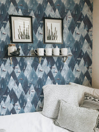 Geometric mountain wallpaper with black frames and white pillows in bedroom.