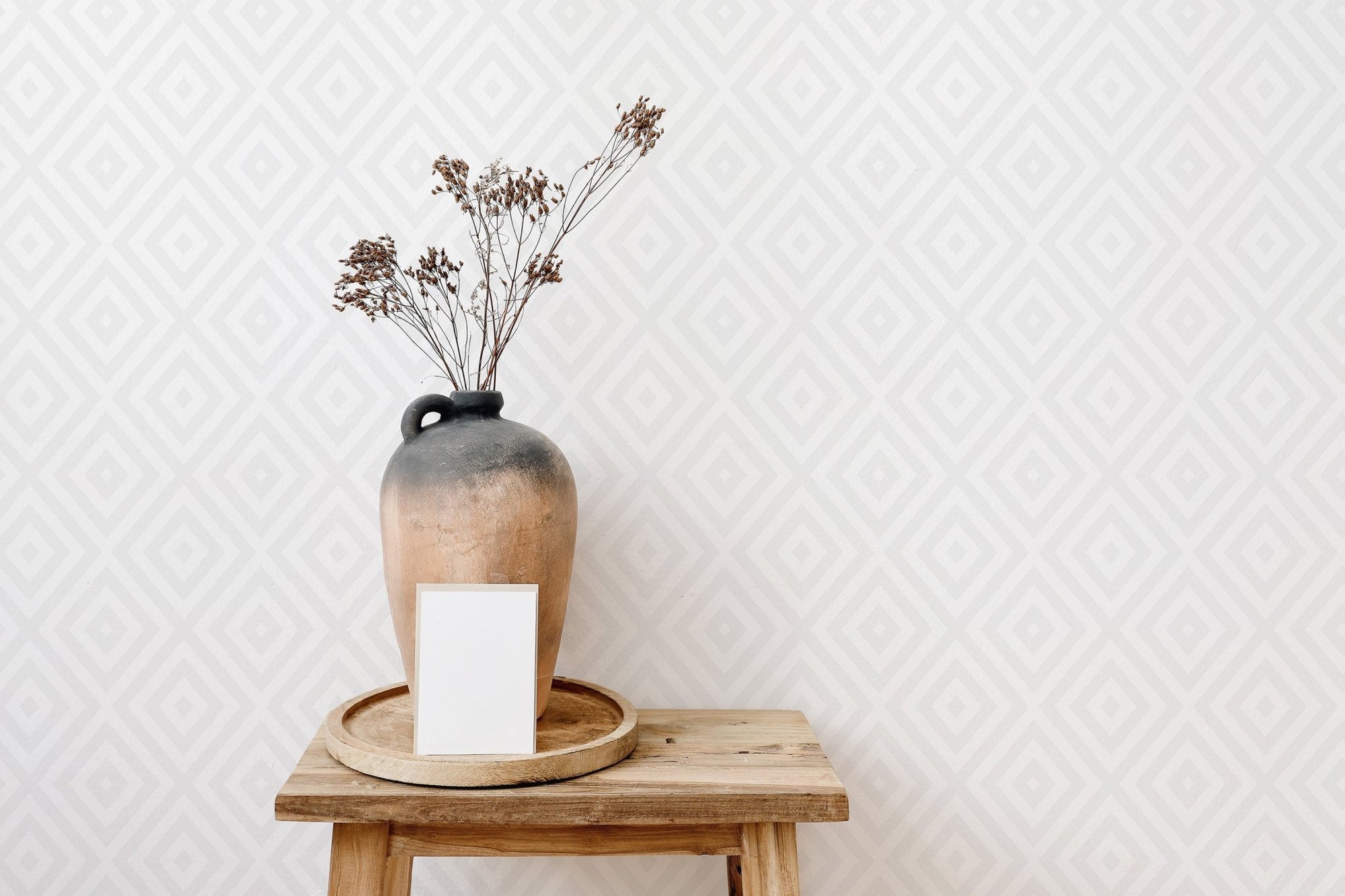 Minimalist earthen vase on wooden stool with diamond pattern wallpaper.