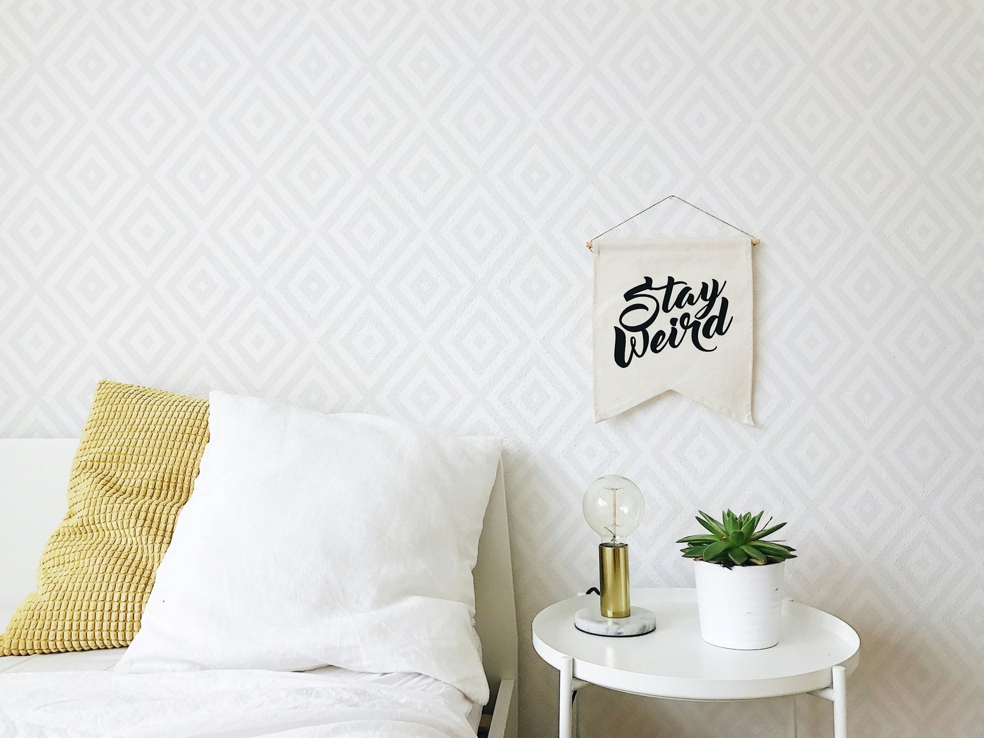 White bedding and side table placed before a gray concentric diamond wallpaper.