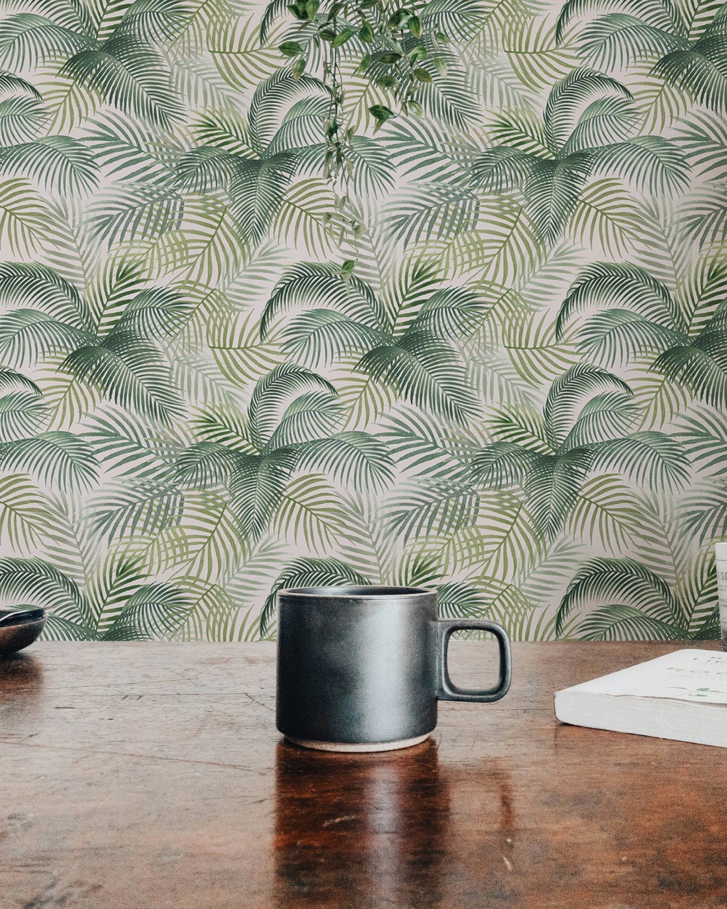 Botanical leaves wallpaper behind a dark ceramic mug on a rustic wooden table.