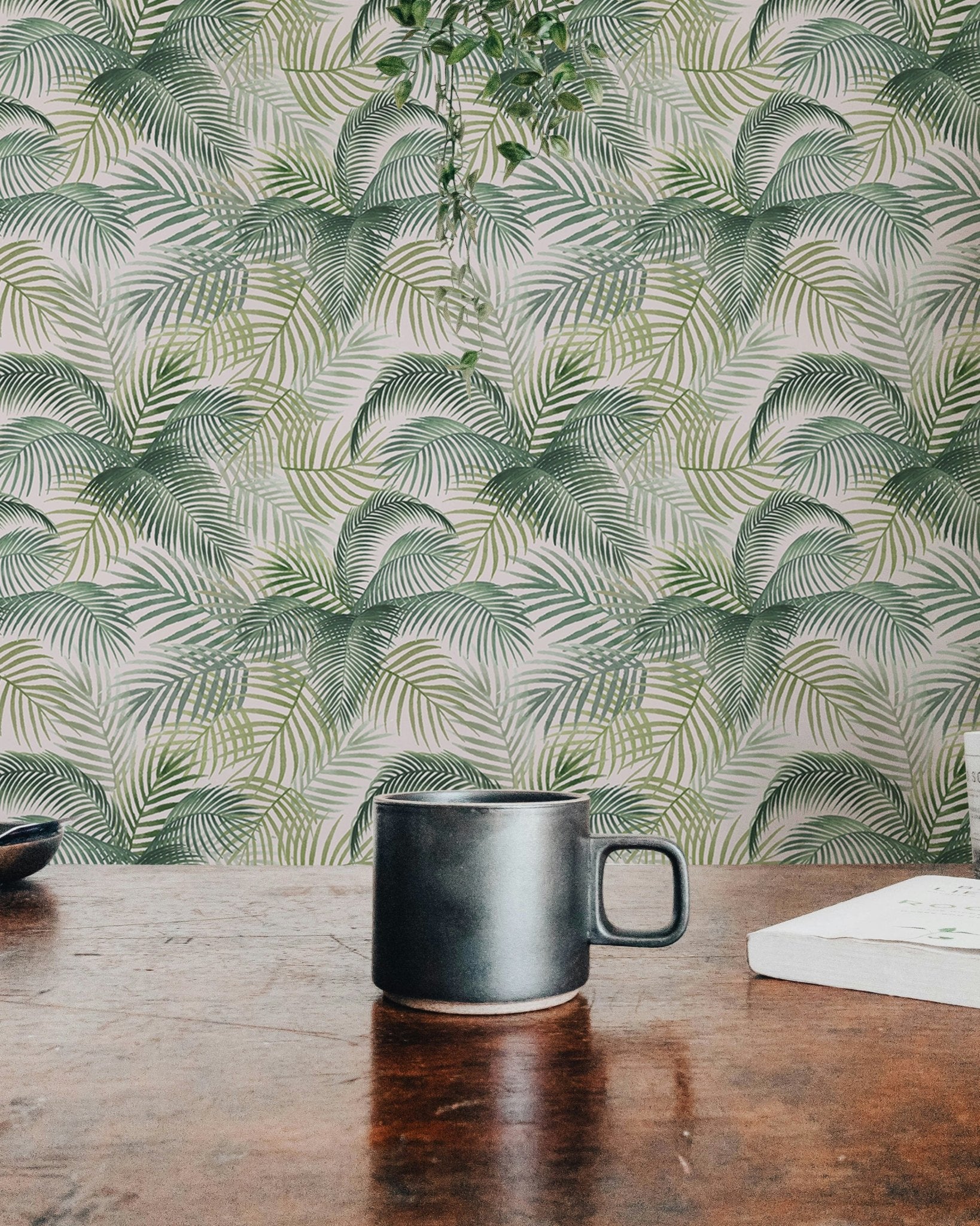 Botanical leaves wallpaper behind a dark ceramic mug on a rustic wooden table.