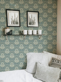 Sage green baroque wallpaper in a living room featuring white pillows and frames.