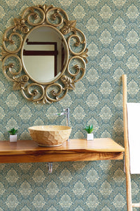Patterned green wallpaper in a bathroom behind a wooden vanity and stone sink.