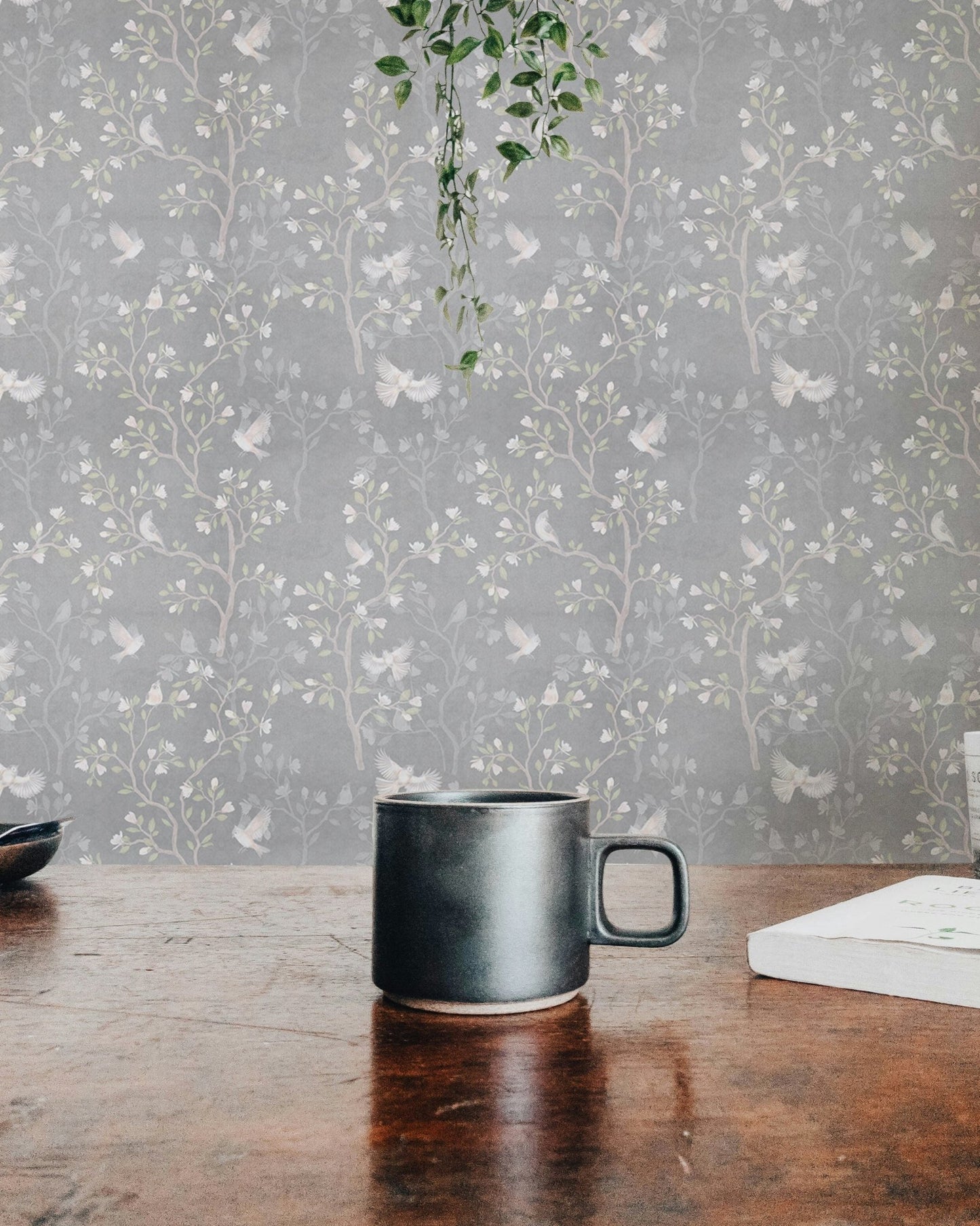 Magnolia tree and birds wallpaper behind a wooden console with small plants.