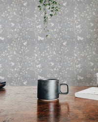 Magnolia tree and birds wallpaper behind a wooden console with small plants.