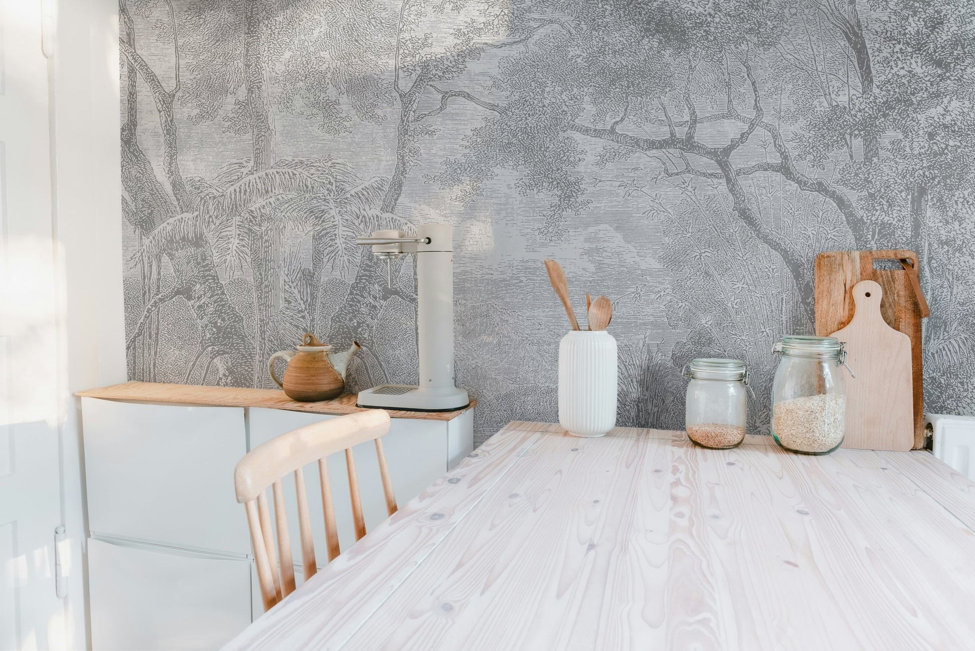 Monochrome forest sketch wall mural behind a white kitchen dining table.