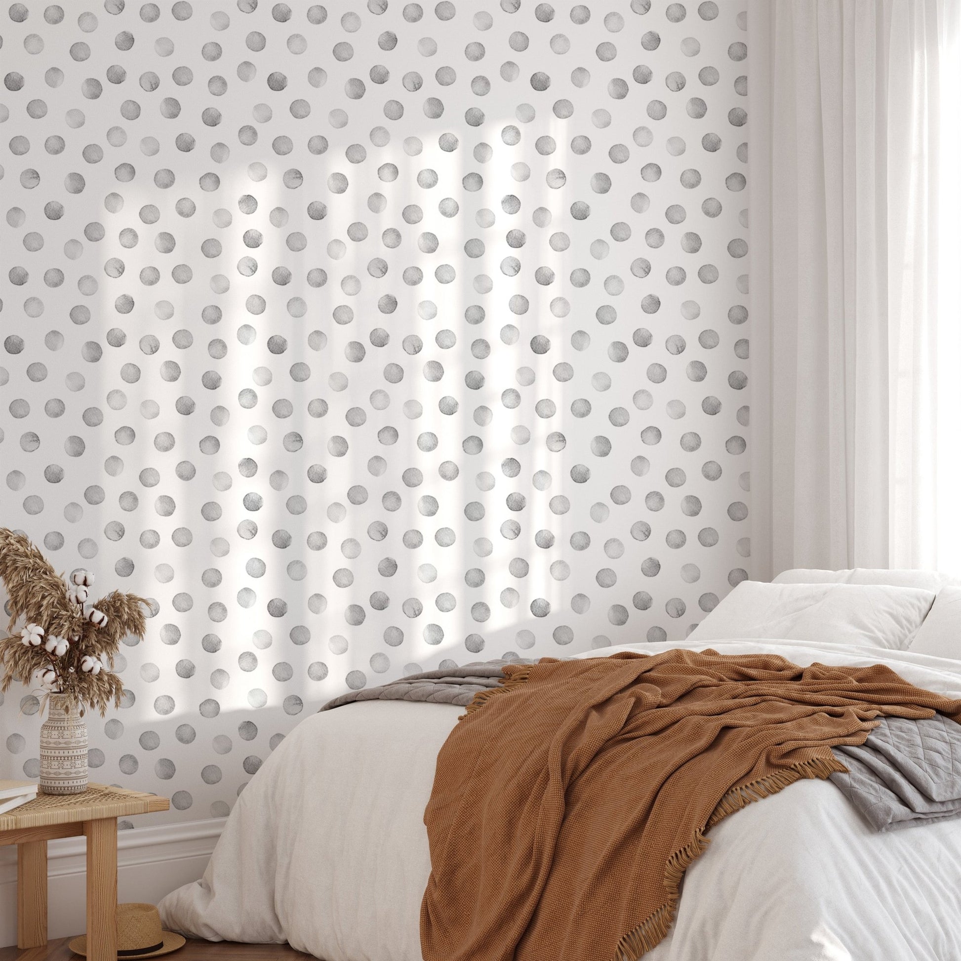 Sunlit bedroom featuring a grey polka dot wallpaper behind white bedding.