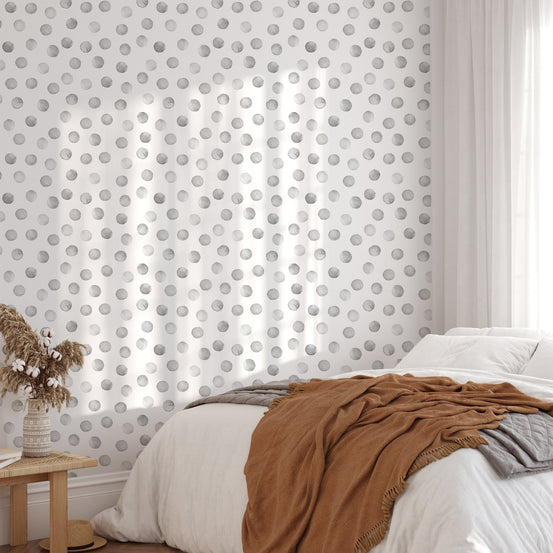 Sunlit bedroom featuring a grey polka dot wallpaper behind white bedding.