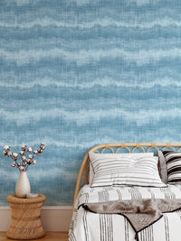 Blue textured wavy stripe wallpaper as a bedroom backdrop for a single bed.