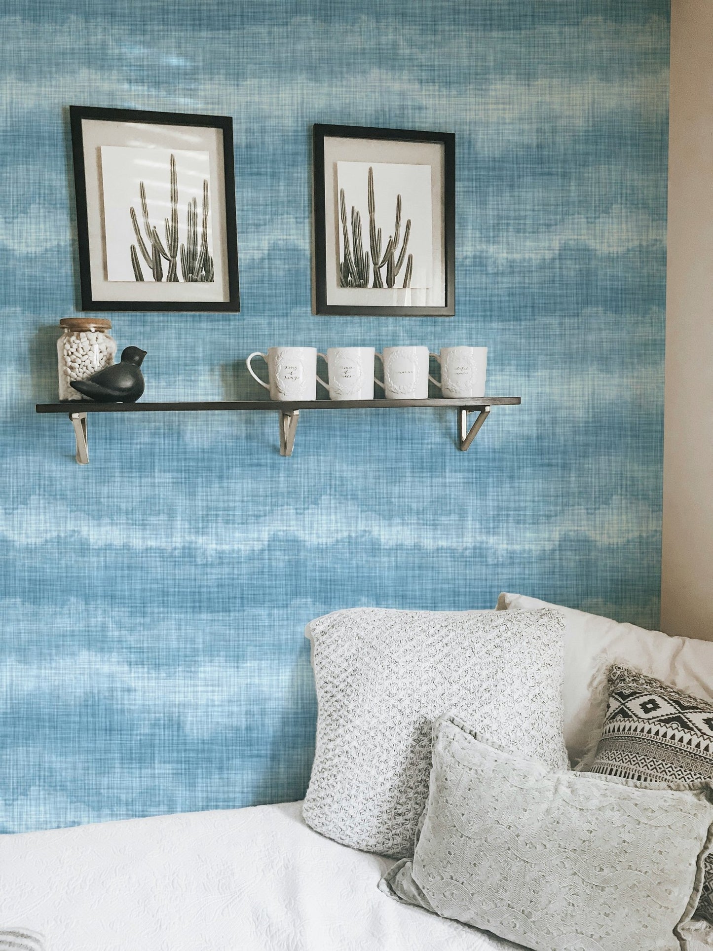 Blue wavy stripe wallpaper in a small bedroom with framed wall art.
