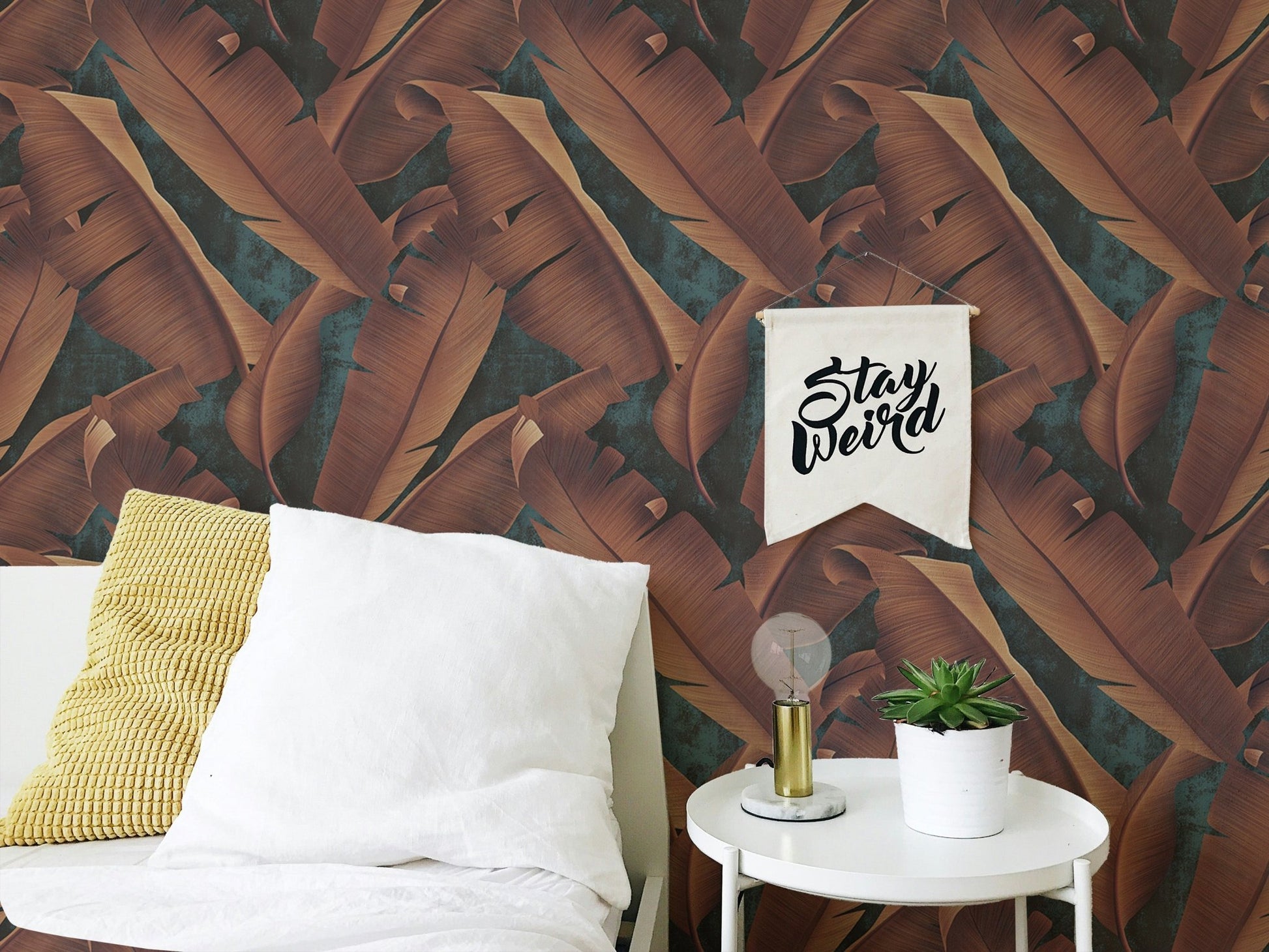 Brown leaves wallpaper in a bedroom with white pillows and a side table.