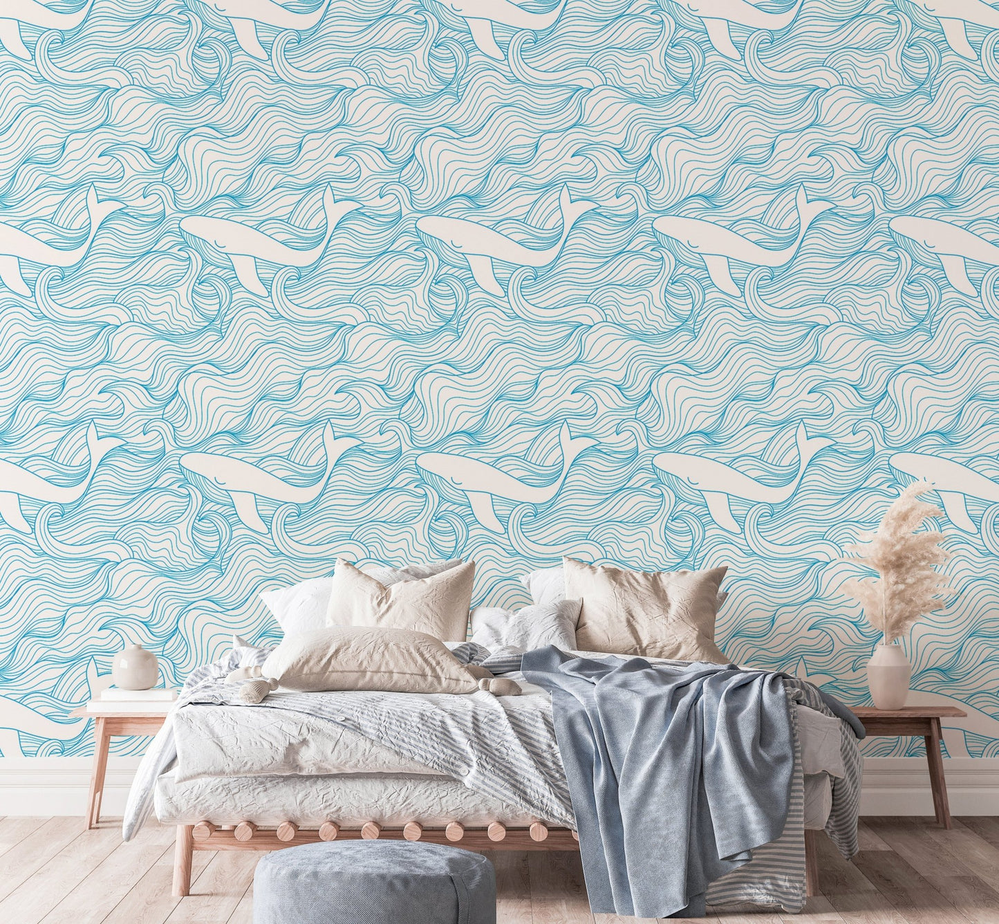 Wave and whale pattern wallpaper behind a bed with neutral linens and pillows.