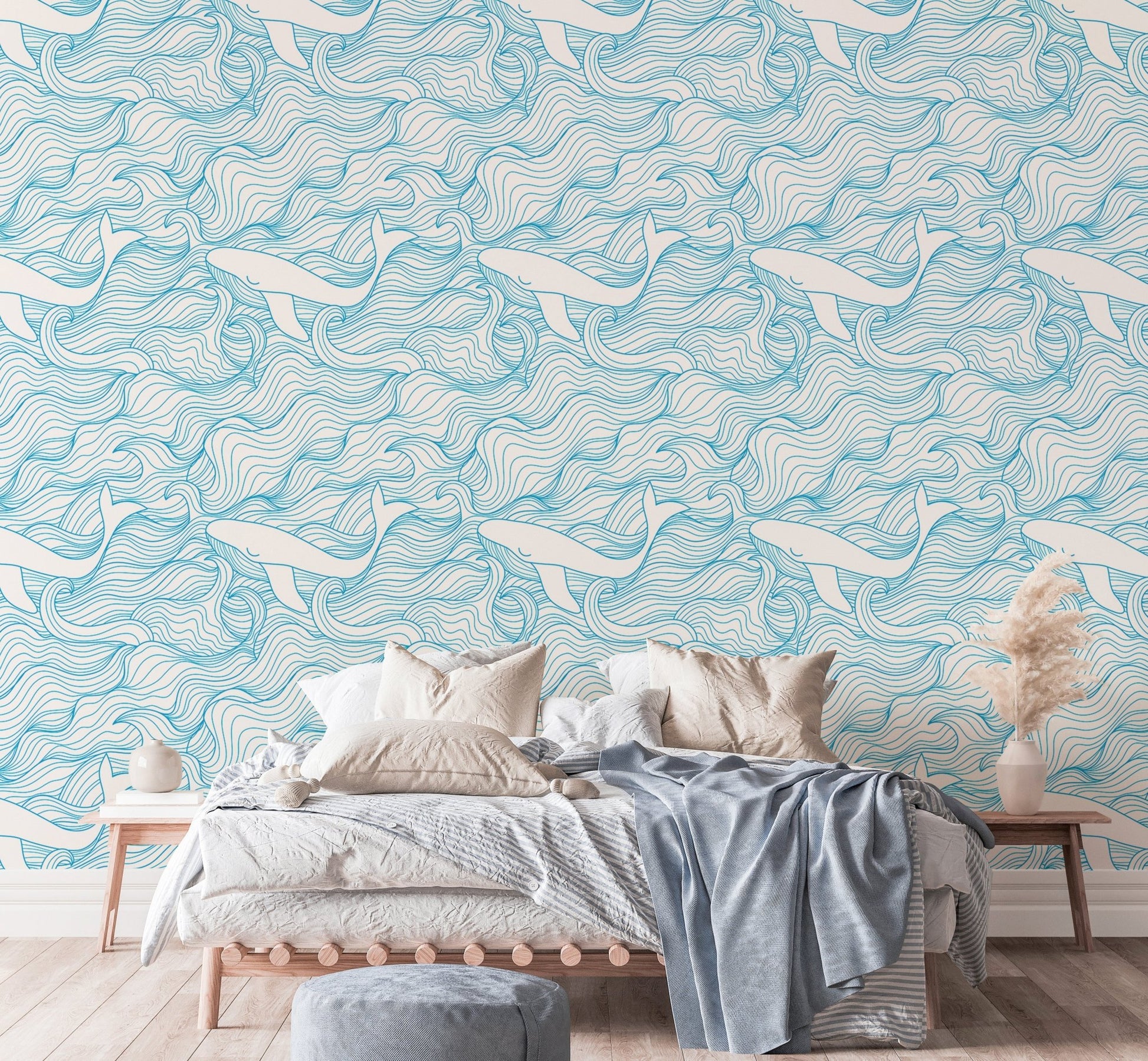Wave and whale pattern wallpaper behind a bed with neutral linens and pillows.