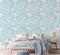 Wave and whale pattern wallpaper behind a bed with neutral linens and pillows.