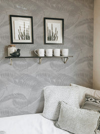 Living room corner with sofa and light gray palm leaves silhouette wallpaper.