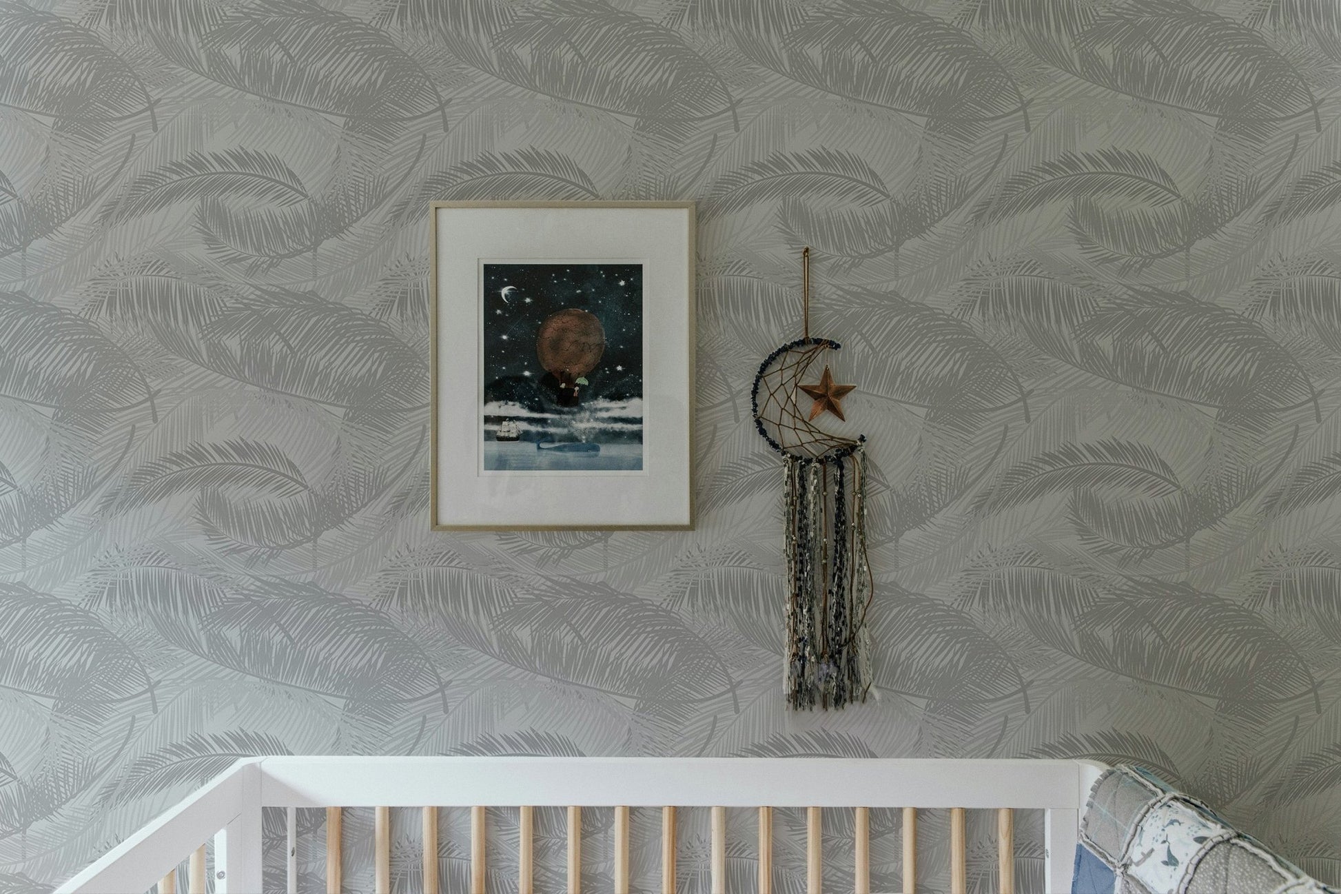 Nursery setting with white crib and light gray palm leaves silhouette wallpaper.