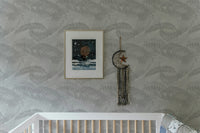 Nursery setting with white crib and light gray palm leaves silhouette wallpaper.
