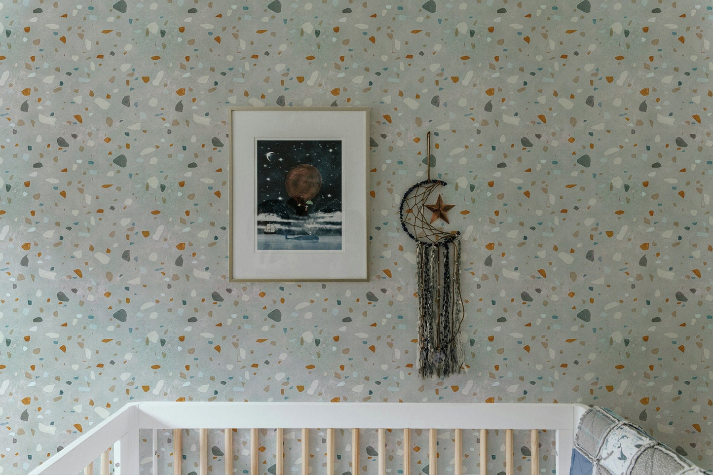 Terrazzo wallpaper in a nursery with a white crib and framed wall art.