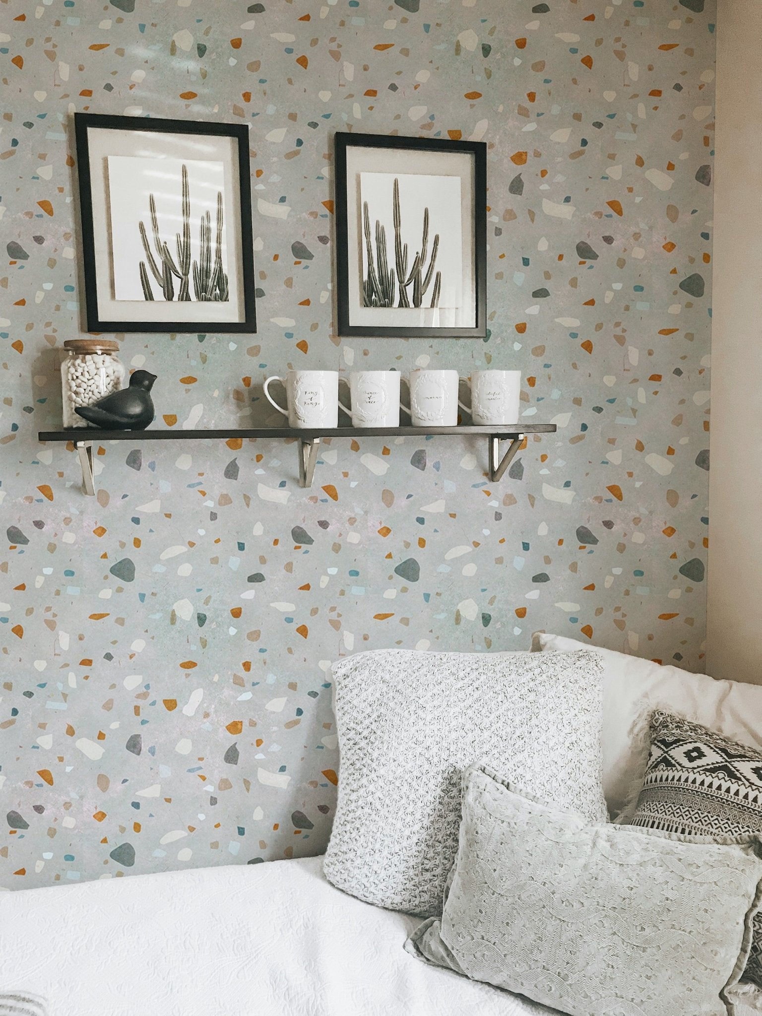 Terrazzo wallpaper with grey and terracotta flecks behind two black framed pictures.