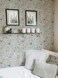 Terrazzo wallpaper with grey and terracotta flecks behind two black framed pictures.