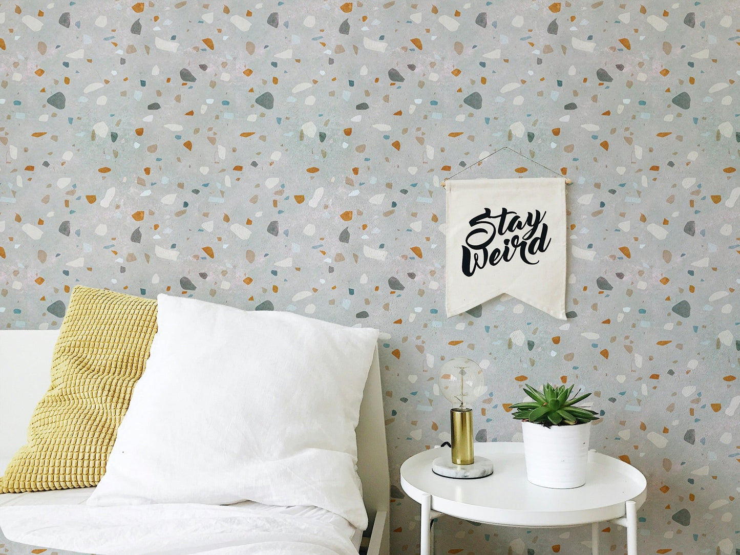 White bed with yellow pillow in front of a mid century modern terrazzo wallpaper.