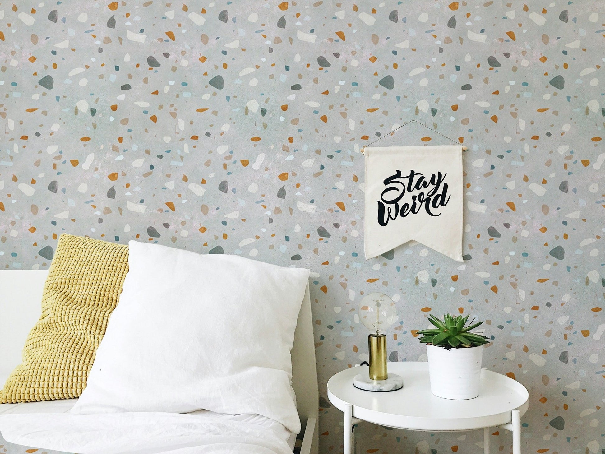 White bed with yellow pillow in front of a mid century modern terrazzo wallpaper.