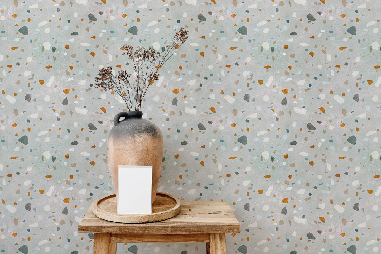 Natural terrazzo wallpaper behind a wooden stool with a ceramic vase and dried flowers.