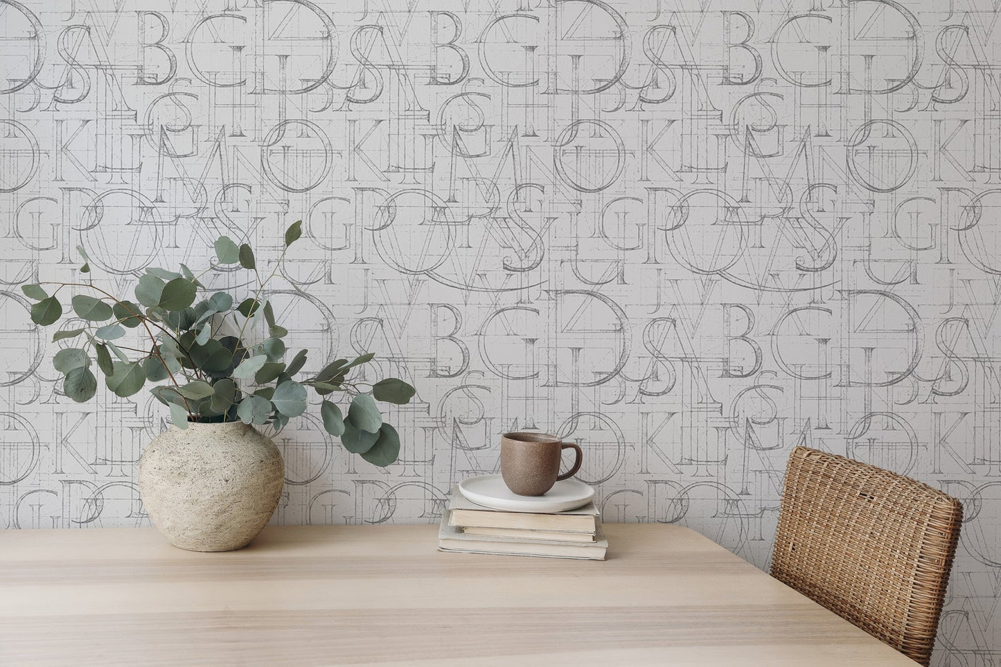 Geometric alphabet wallpaper behind a wooden dining table with a ceramic vase.