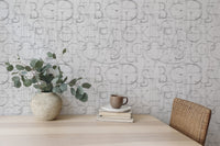 Geometric alphabet wallpaper behind a wooden dining table with a ceramic vase.