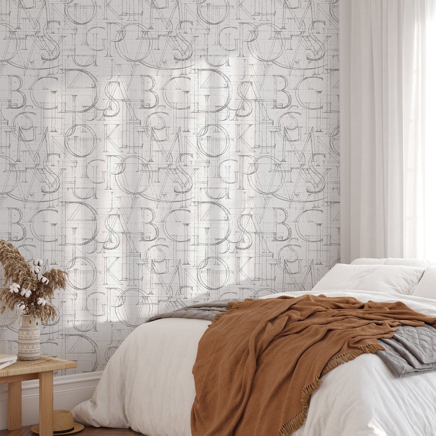 Geometric alphabet wallpaper in a bedroom with a terracotta throw and sunlight shadows.