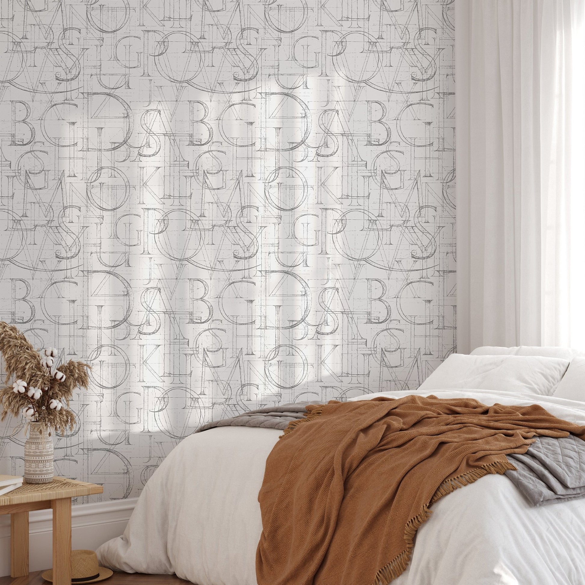 Geometric alphabet wallpaper in a bedroom with a terracotta throw and sunlight shadows.