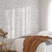Geometric alphabet wallpaper in a bedroom with a terracotta throw and sunlight shadows.
