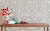 Symmetrical line pattern wallpaper behind a wooden bench with pink flowers.